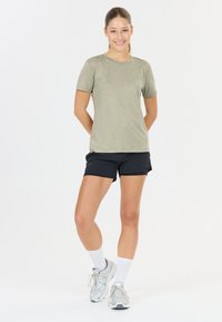 Licht olijfgroen t-shirt met korte mouwen en een ronde halslijn, gecombineerd met zwarte sportshorts. Model draagt witte sokken en zilveren sneakers.