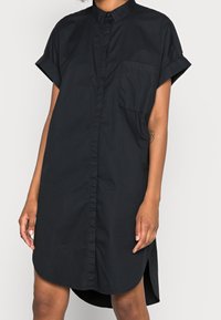 Abito camicia nero a maniche corte con chiusura a bottoni, taschino sul petto e orlo curvo. Realizzato in un tessuto leggero e morbido.