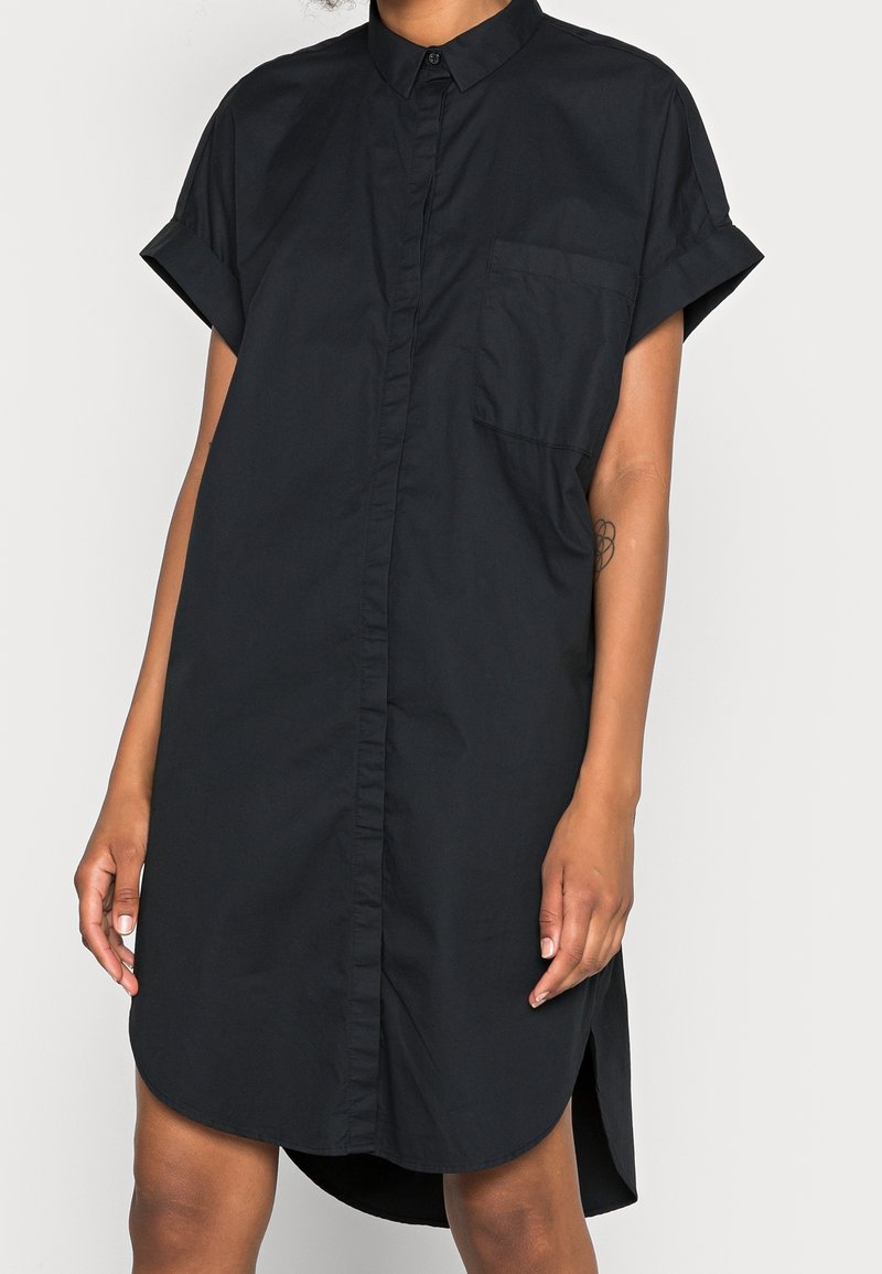 Abito camicia nero a maniche corte con chiusura a bottoni, taschino sul petto e orlo curvo. Realizzato in un tessuto leggero e morbido.