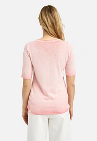 Helles rosa T-Shirt mit kurzen Ärmeln, runden Ausschnitt, weicher Textur und leicht abgerundetem Saum. Mit seitlichen Schlitzen für mehr Bewegungsfreiheit gestaltet.