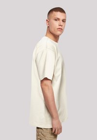 Light beige short-sleeve t-shirt with a relaxed fit, round neckline, and distinctive seam detailing on the shoulders.
