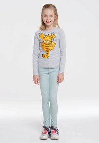 Graues Langarmshirt mit einem Cartoon-Katzenmotiv, kombiniert mit hellblauen Skinny-Jeans und bunten Sneakers mit gemusterten Schnürsenkeln.