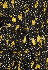 Vestido de tela negra con un patrón de flores amarillas y lunares blancos, con una cintura fruncida y detalles de botones en la parte delantera.