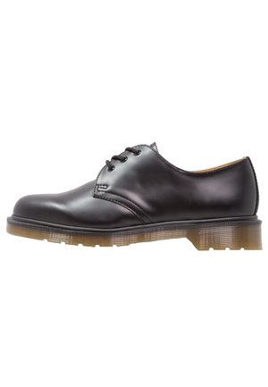 Chaussure en cuir noir avec bout arrondi, design à lacets, et semelle transparente texturée. Fini lisse avec des détails minimalistes de coutures.