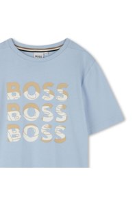 Camiseta de algodón azul claro con texto repetido "BOSS" en beige y blanco. Cuello redondo clásico y mangas cortas. Textura suave.