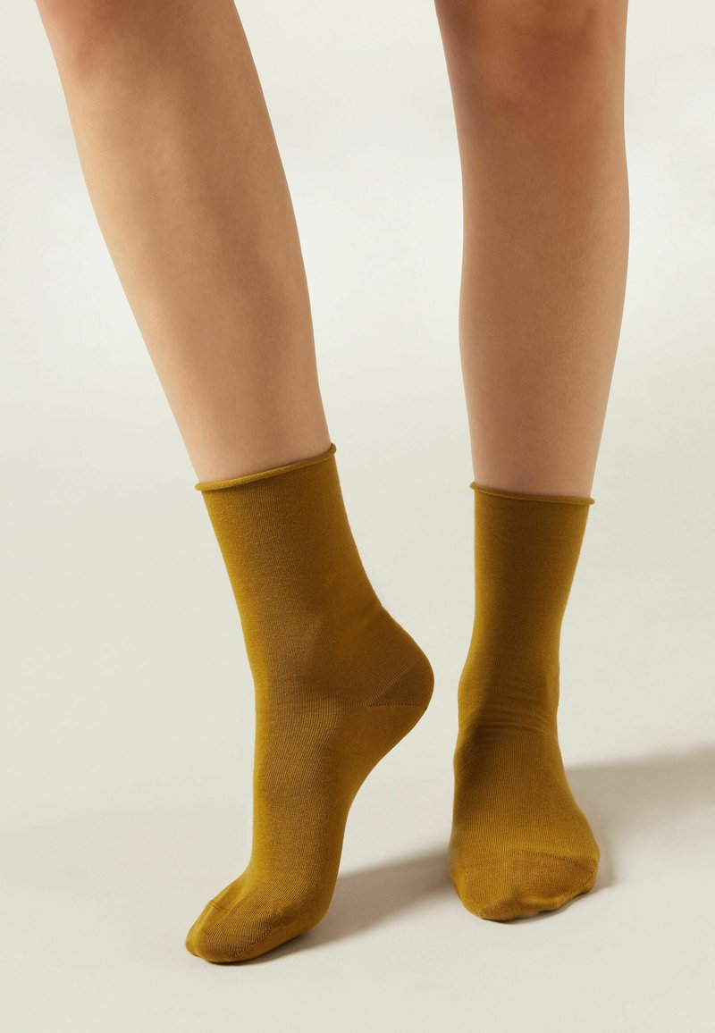 Calcetines de tobillo color mostaza, con textura suave, forma tubular, y con un puño acanalado. Se ajustan de cerca al tobillo sin adornos.