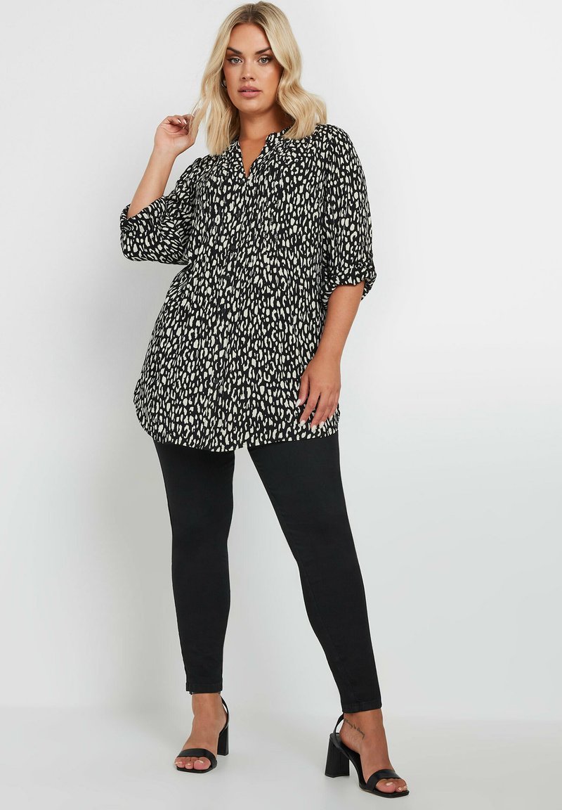 Schwarze und weiße Tierdruckbluse mit Knopfleiste, dreiviertelärmeln und lockerer Passform, kombiniert mit schwarzen Skinny Jeans und schwarzen Absätzen.