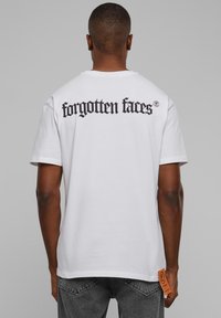 Valge puuvillane t-särk, millel on musta gooti stiilis tekst "forgotten faces" tagaküljel. Küljel on oranž silt.