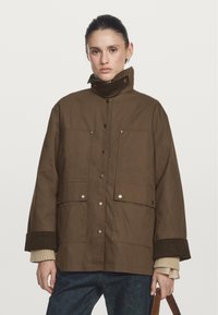 Braune, isolierte Jacke mit hohem Kragen, ausgestattet mit Druckknöpfen, großen Fronttaschen und gerippten Bündchen. Glatte Textur, lässige Passform.