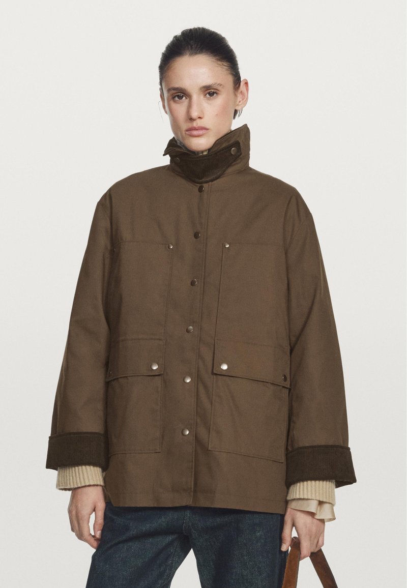 Braune, isolierte Jacke mit hohem Kragen, ausgestattet mit Druckknöpfen, großen Fronttaschen und gerippten Bündchen. Glatte Textur, lässige Passform.