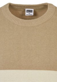 Pull beige avec un col rond nervuré. Présente une bande crème horizontale sur la partie inférieure. Fabriqué en matériau tricoté texturé.