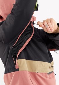 Personne dézippant la fermeture éclair de ventilation noire et rose du blouson sous le bras, révélant la doublure intérieure en mesh noir.