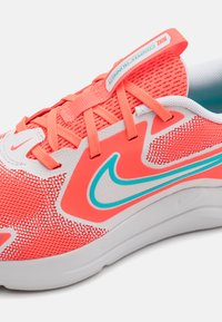 Crveno-bijela tenisica s mrežastim gornjim dijelom, tirkiznim detaljima i podstavljenim jezikom. Čipke su svijetlo narančaste. Nike logotip je vidljiv.