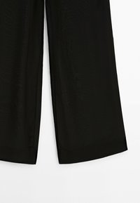Pantalon noir à jambes larges avec une texture de tissu douce, présenté de la mi-cuisse à l'ourlet sur un fond blanc uni.