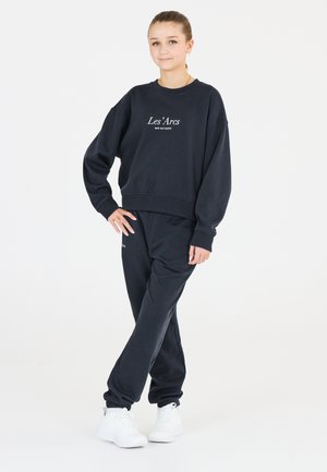 Mørk marineblå sweatshirt og joggers sæt lavet af en bomuldsblanding, med en rund hals og broderet tekst. Kombineret med hvide sneakers.