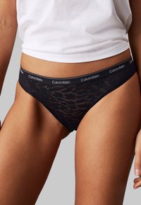 Svart blonde thong med en elastisk midje fra Calvin Klein. Designet har et subtilt mønster og en lavere skjæring.