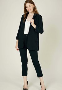 Blazer noir avec un col noté, des manches longues et deux poches avant, associé à un pantalon noir slim et des escarpins noirs à bout pointu.