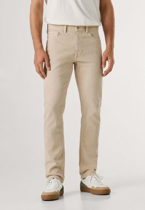 Beige denimjeans med en slank pasform, femlomme-design og metalbeslag, kombineret med hvide og grønne sneakers.