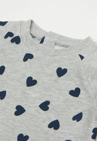Sweatshirt gris avec des motifs de cœurs navy, col côtelé et détail de bouton au dos. Matériau en coton doux.