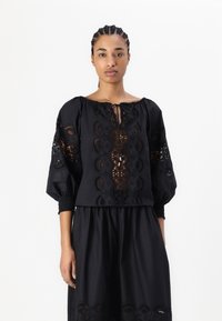Blusa nera con dettagli in pizzo intricati, maniche a palloncino e scollatura con coulisse. Realizzata in tessuto leggero con una finitura testurizzata.