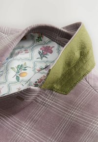 Pflaumenfarbener Karostoff mit grünem Filzkragen; das Innenfutter hat ein Blumenmuster auf weißem Hintergrund mit gewelltem Rand.