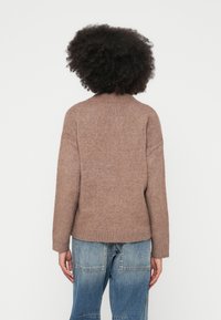 Camisola castanha de malha com gola e punhos canelados, apresentando um corte descontraído. Usada com jeans azuis, vista por trás.