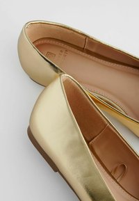 Ballerines en métal doré avec une finition lisse, des orteils ronds et un subtil détail de rembourrage intérieur. Semelle plate et design minimaliste.