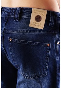 Jeans aus Denim in einem tiefen Blauton mit einem Lederetikett, auf dem "Picaldi Jeans Authentic Design" steht. Zu den Merkmalen gehören Kupferriegel und ein klassischer Schnitt.