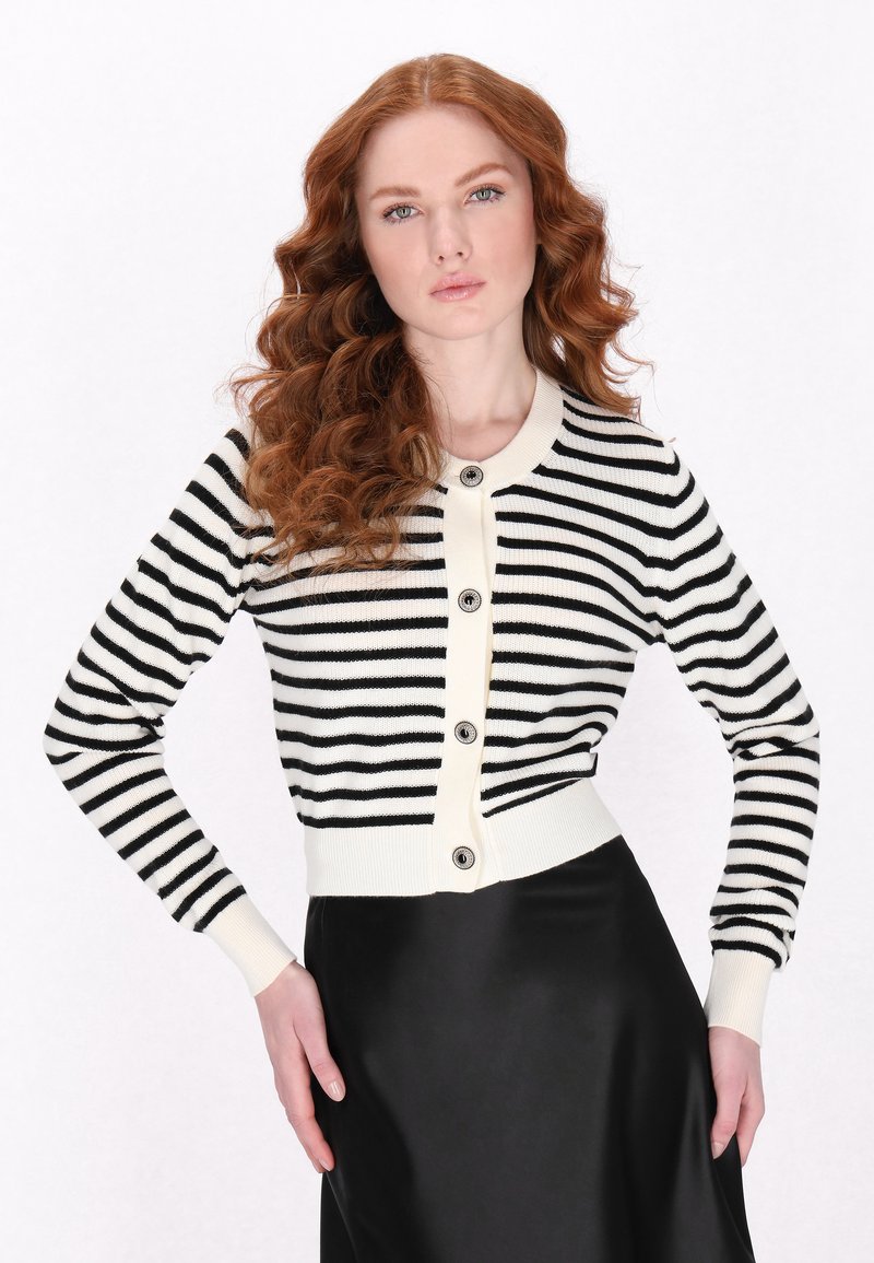 Cardigan a righe bianco e nero con scollo arrotondato, chiusura con bottoni e polsini a coste, indossato sopra una gonna nera. Tessuto a maglia liscia.