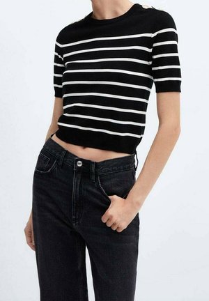 Kobieta w czarno-białej koszulce w poziome paski z krótkim rękawem i złotymi guzikami na ramieniu, zestawiona z czarnymi jeansami z wysokim stanem.