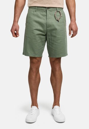 Mand iført lysegrønne knælange shorts med fletnet nøglering og hvide sneakers mod en hvid baggrund.