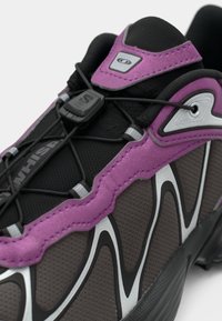 Shoe featuring a textured black base with purple accents, silver wave patterns, and a lace-lock system for a secure fit.