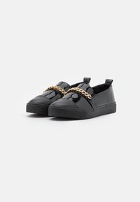 Black patent leather slip-on shoes with a thick rubber sole, featuring a gold chain accent across the front and pull tabs at the heel.