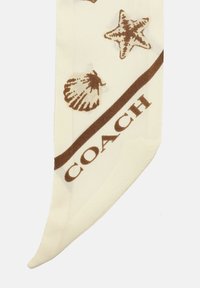 Crèmesjaal met bruine schelpen- en zeesterrenpatronen, met het woord "COACH" in een vet, donker lettertype aan de onderrand.