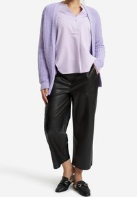 Kobieta w fioletowym kardiganie i bluzce, czarnych skórzanych spodniach typu cropped oraz czarnych mokasynach z futrzanym wykończeniem.