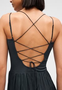 Vestido negro con corpiño acanalado y diseño de tirantes cruzados en la espalda, falda fluida y detalle de lazo ajustable.