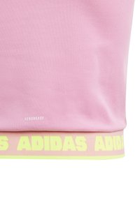 Αθλητική μπλούζα σε ανοιχτό ροζ απόχρωση με ριγωτή υφή, διαθέτει κίτρινη λωρίδα με το λογότυπο "ADIDAS" στο κάτω μέρος και την ένδειξη "AEROREADY" εκτυπωμένη πάνω από το τελείωμα.