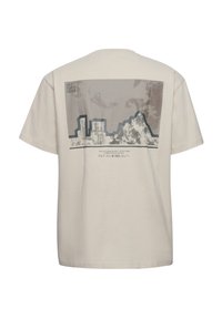 Beige T-shirt met afbeelding van stadsgebouwen en berglandschap op de achterkant, inclusief de tekst "OFF DUTY GEAR" en "HALO".