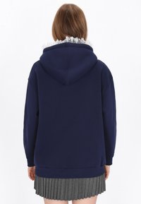 Sudadera con capucha azul marino con un forro gris con volantes alrededor de la capucha, mangas largas y un corte relajado, combinada con una falda gris plisada.