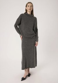 Maglione lavorato a maglia grigio con collo alto e vestibilità ampia, abbinato a una lunga gonna coordinata. Il tessuto sembra morbido e testurizzato. Scarpe nere con punta.