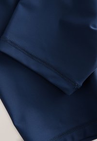 Mørkeblå, glat stof med mat finish. Har flade syninger og et rent design uden synlige mønstre eller accenter.