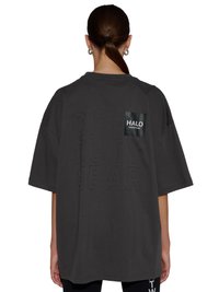 Femme aux cheveux bruns attachés en queue de cheval portant un t-shirt noir ample avec un texte en relief "OFF DUTY GEAR" et un petit patch "HALO" dans le dos.