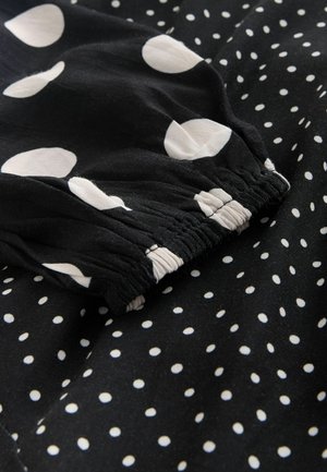 Czarna tkanina z dużymi białymi kropkami i mniejszymi kropkami polka. Szczegół elastycznego pasa z marszczoną fakturą. Miękki, lekki materiał.
