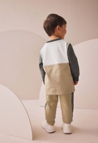 Beige and gray two-tone long-sleeve shirt with a curved hem, paired with beige pants featuring gray side panels, and white sneakers.