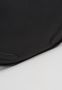 Borsa nera in pelle con superficie testurizzata, forma arrotondata e dettaglio logo in rilievo. Design minimalista con sottili accenti di cucitura.