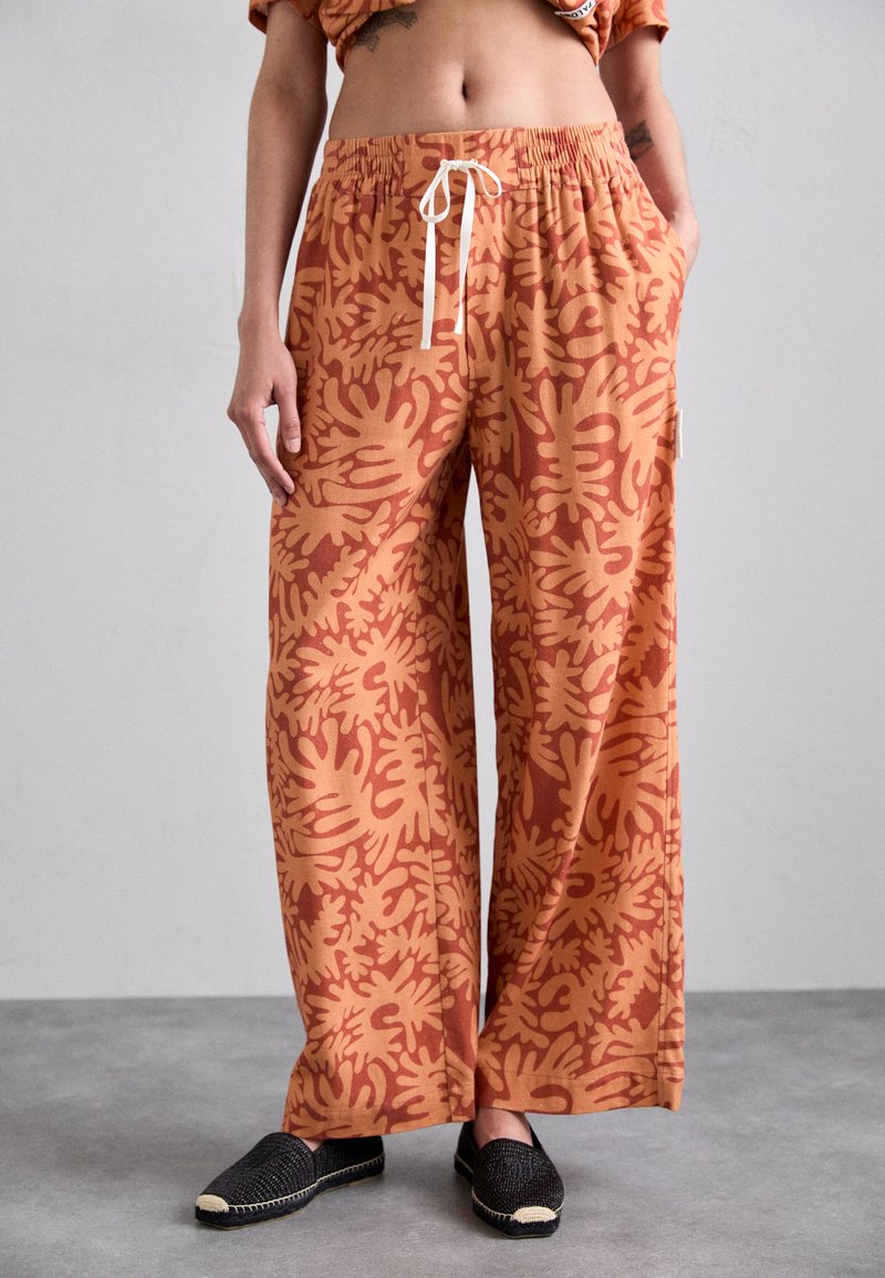 Wide-leg pants in burnt orange with a textured leaf-pattern design. Features an elastic waistband with a drawstring and side pockets.