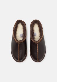 Dark brown leather slippers with a soft shearling lining, featuring contrasting tan stitching and a rounded toe design.