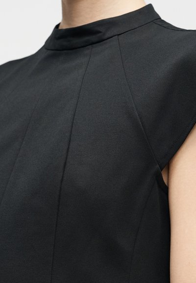 Juodas, struktūruotas viršus su aukštu kaklu ir trumpomis rankovėmis. Turi vertikalias siūles ir lygų, šiek tiek tekstūruotą audinį.