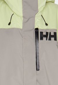 Helle graue und neongrüne wasserdichte Jacke mit einer Reißverschlusstasche, verstellbarem Kapuzen und auffälligem schwarzen Branding auf der Vorderseite.