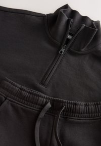 Sweat-shirt noir à col zippé avec col côtelé et pantalon de survêtement à cordon sombre, doté d'une ceinture élastique et d'une texture douce.
